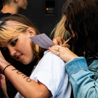 Jugendliche schreiben etwas auf Postkarten und benutzen den gegenseitigen Rücken als Lehne um das Aufschreiben zu vereinfachen