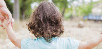 Man sieht ein Kleinkind von hinten. Es hält zwei Hände in der Hand und zusammen gehen die drei Personen durch den Wald