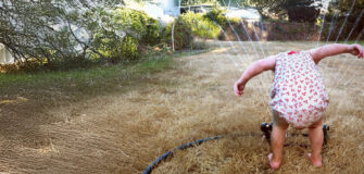 Kleinkind hält den Kopf über einen Schlauch der Wasser sprenkelt