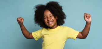 Kind lächelt in die Kamera und hält Arme in die Höhe