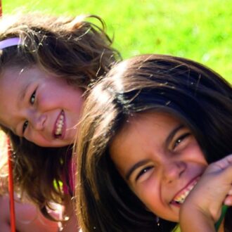 Vier Kinder sitzen auf einer Schaukel und lächeln in die Kamera