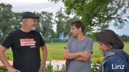 Erich Fenninger unterhält sich mit zwei Besucher*innen, im unteren rechten Abschnitt des Bildes steht "Linz"