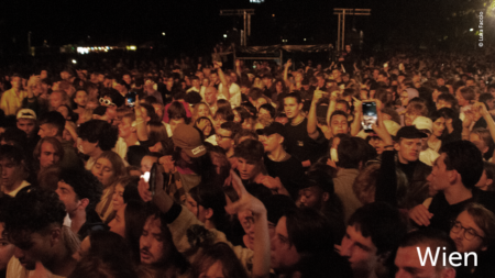 Das Publikum vor der Bühne. Einige halten Handys in die Höhe, um das Event zu filmen. Im unteren rechten Abschnitt des Bildes steht: "Wien"