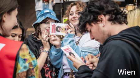Jugendliche/Junge Erwachsene füllen den Volkshilfe Flyer aus. Zwei Frauen lächeln in die Kamera, im unteren rechten Abschnitt des Bildes steht "Wien"