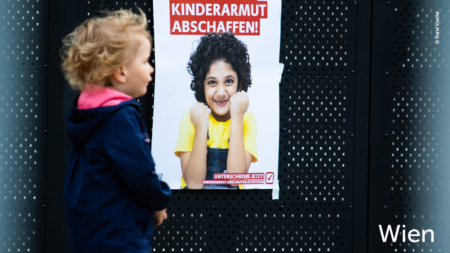 Ein Kleinkind läuft an einem Volkshilfe Poster vorbei mit der Aufschrift: "Kinderarmut abschaffen!" Im unteren rechten Abschnitt des Bildes steht: "Wien"