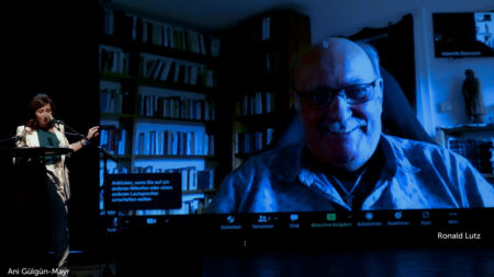 Moderatorin Ani Gülgün-Mayr auf der Bühne, Ronald Lutz über einen VideoCall dabeigeschaltet