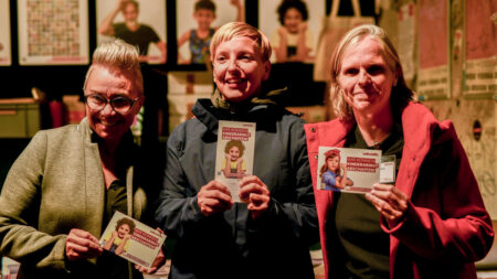 Besuchende halten Postkarten der Volkshilfe in der Hand und lächeln in die Kamera