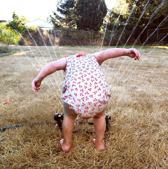 Kleinkind hält den Kopf über eine Sprinkleranlage um sich abzukühlen