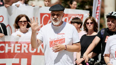 Erich Fenninger hält eine Rede. Im Hintergrund sieht man Beistehende die Banner in den Händen halten