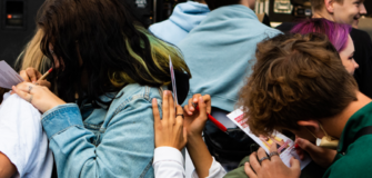 Jugendliche schreiben etwas auf Postkarten und benutzen den gegenseitigen Rücken als Lehne um das Aufschreiben zu vereinfachen