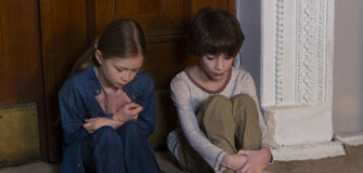 Zwei Kinder sitzen vor einer verschlossenen Tür und schauen traurig auf den Boden